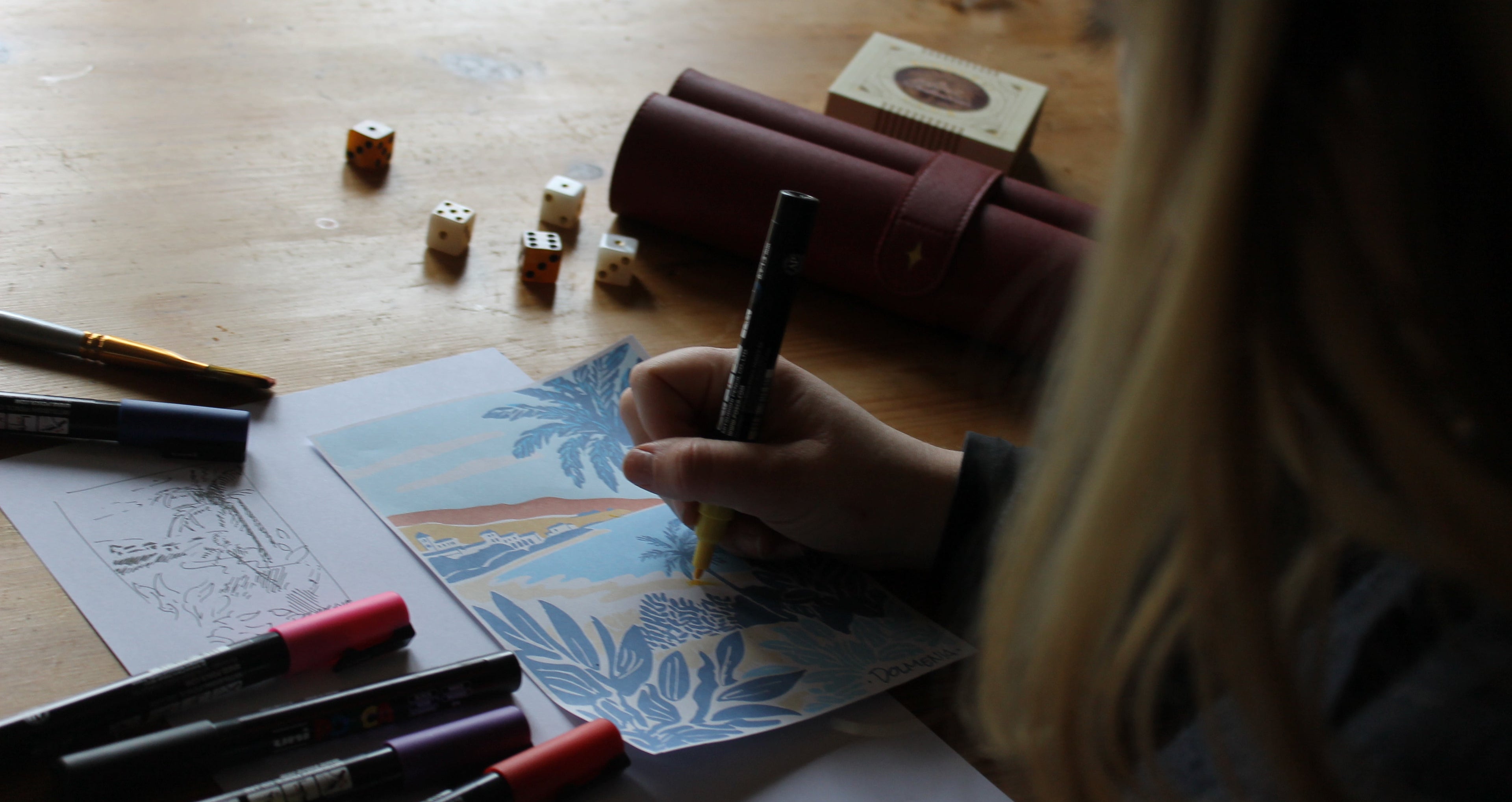 Person drawing on paper with markers on a wooden table