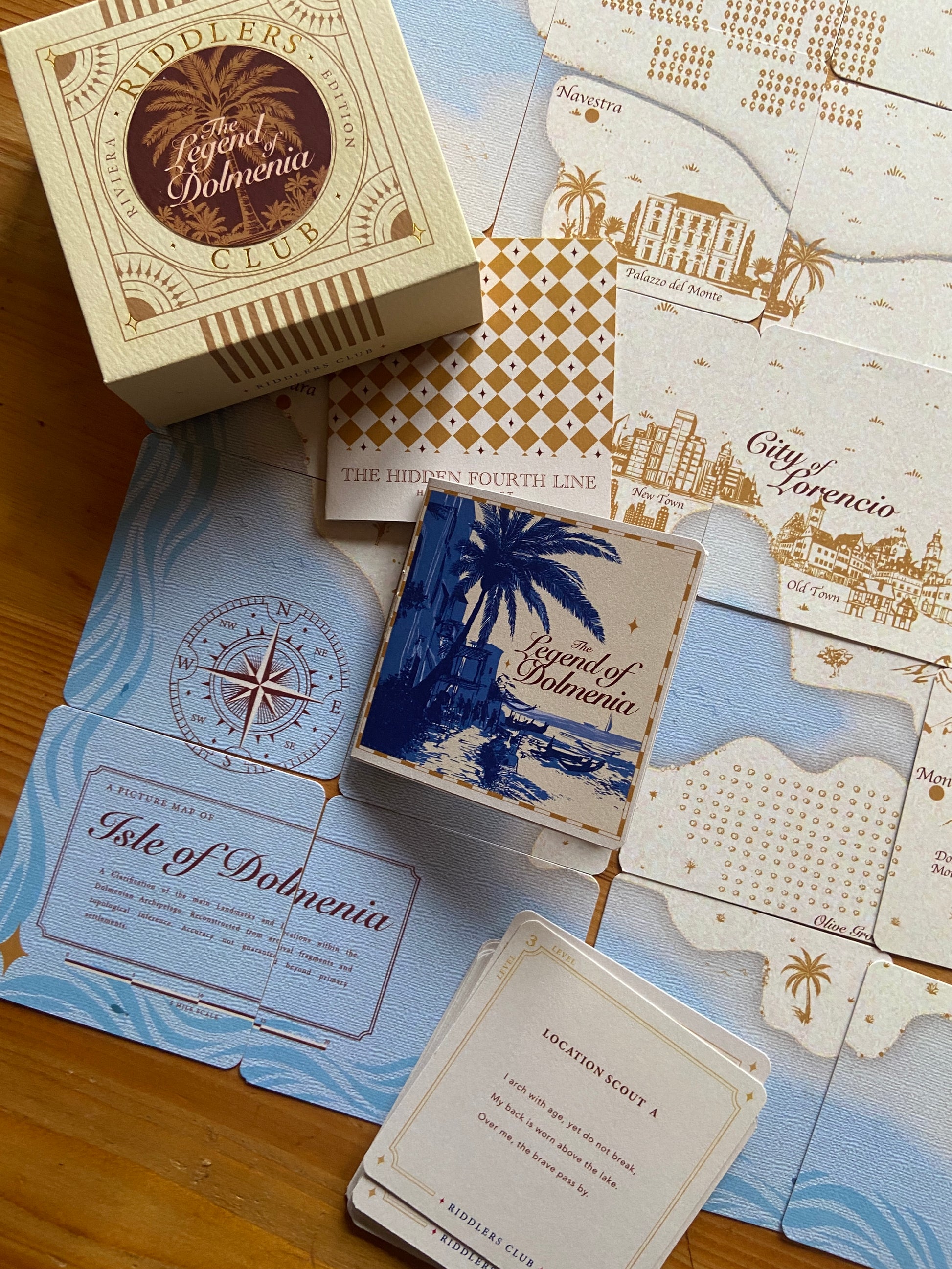 Collection of 'Legend of Dolmenia' cards and packaging on a wooden surface with map designs.